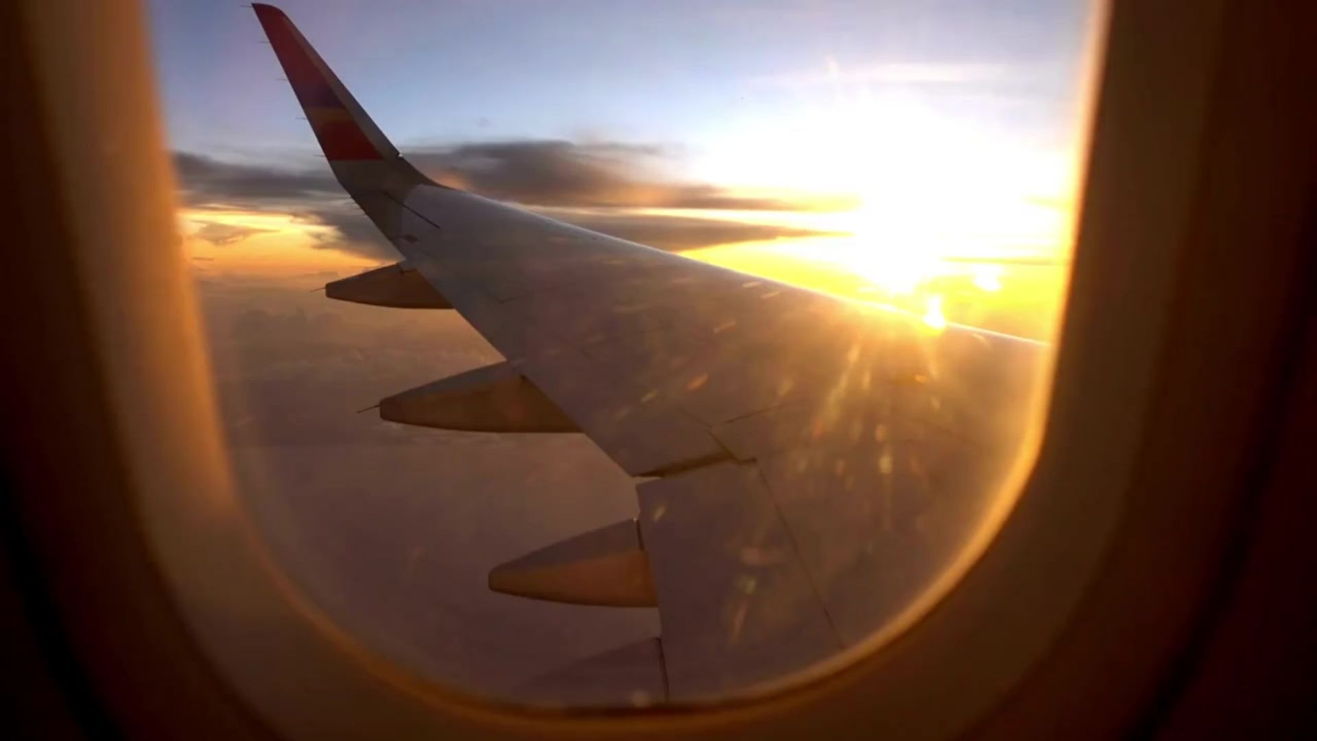View from a private jet cabin window showing the aircraft wing illuminated by golden sunset light above the clouds.